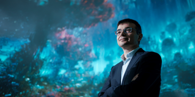 PDG de Google DeepMind devant un écran géant affichant un paysage 3D généré par Genie 2.