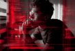 photo du hacker du site Frontière devant son ordinateur avec des lignes de code rouges qui défilent sur l’écran