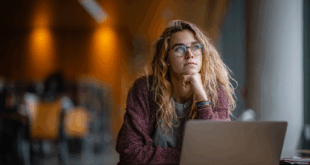 Étudiante concentrée devant son ordinateur dans une bibliothèque, réfléchissant à la rédaction de ses travaux de fin d’études.