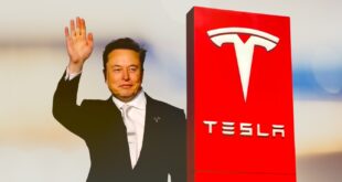 Elon Musk debout à côté d'une plaque Tesla, levant la main