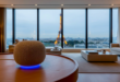 une enceinte Google Home dans une maison offrant une vue panoramique sur la tour Eiffel illustrant l'arrivée de Gemini for Home en France