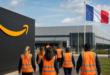 Entrepôt Amazon en France avec employés en gilet de sécurité marchant vers le site, drapeau français.