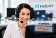 Une femme service client souriant avec son casque devant son ordinateur.
